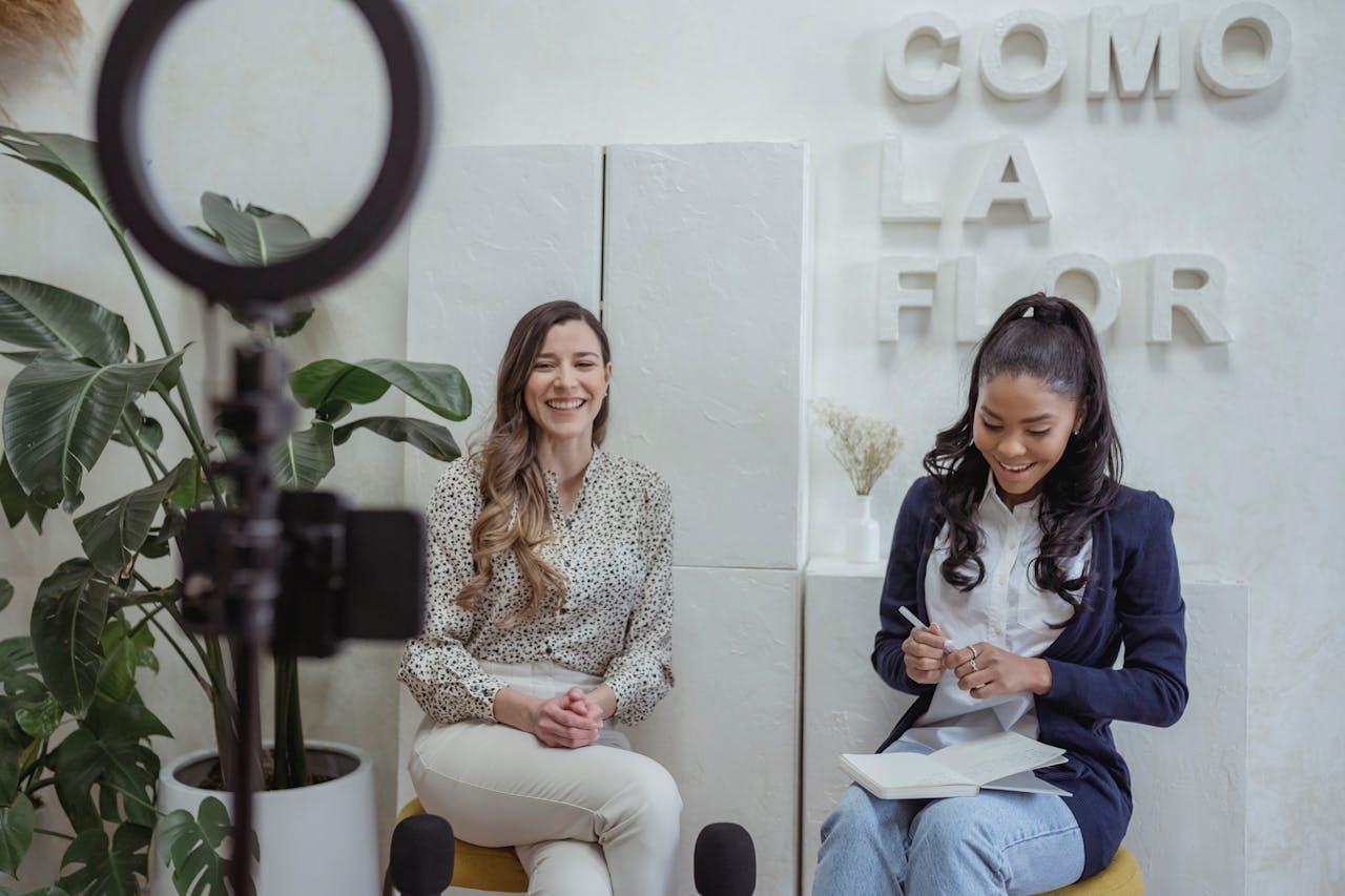 Two women having a lively podcast interview with a stylish indoor setup and microphones.