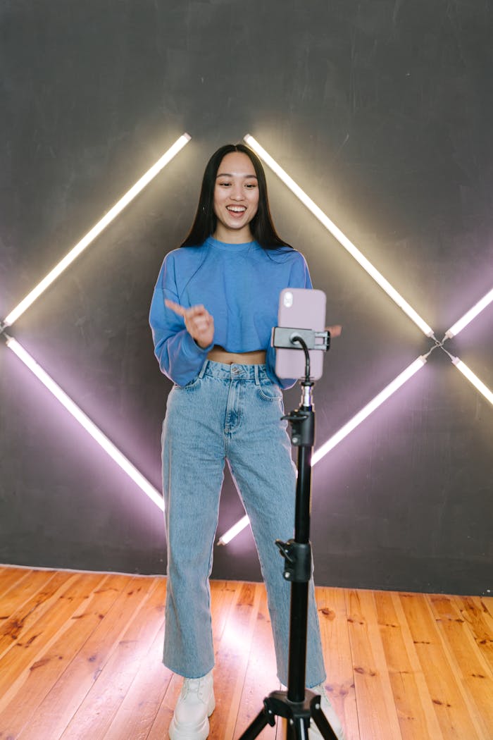 Asian woman vlogging with a phone on tripod in stylish room with geometric lighting.